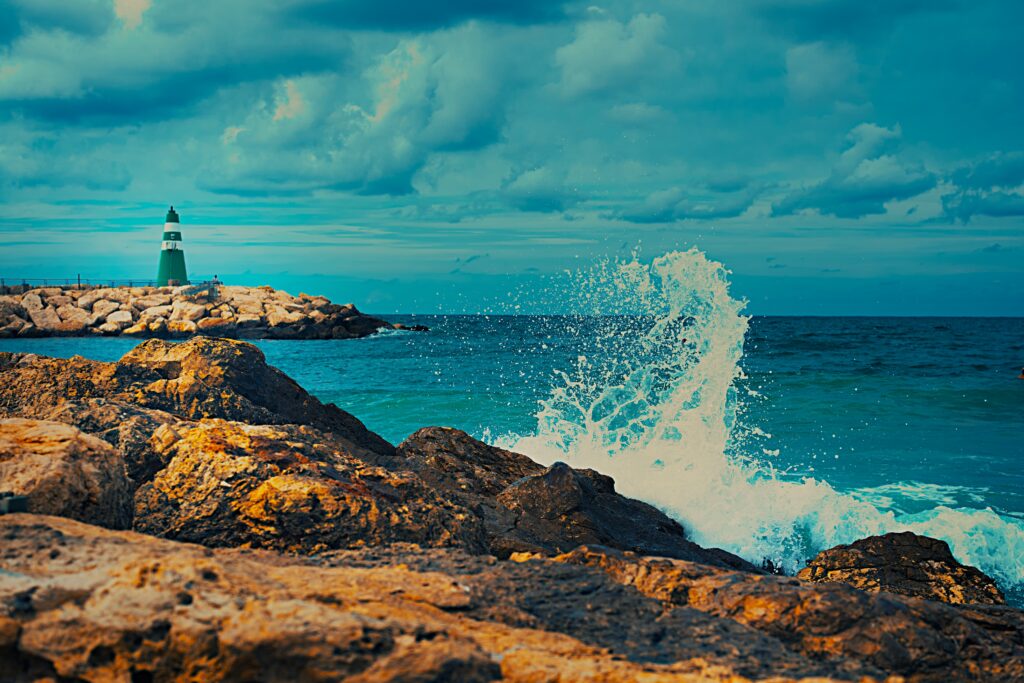 "Green Lighthouse in Tel Aviv." The photograph shows a green lighthouse located on a rocky coastline overlooking the rippling sea.